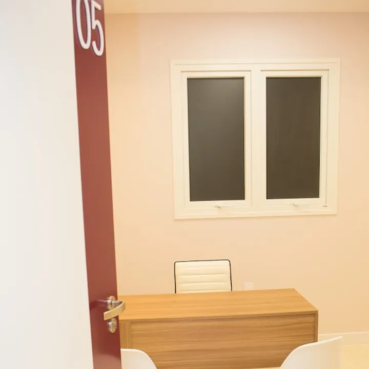 Consultório médico com mesa de madeira e duas cadeiras brancas