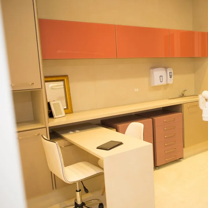 Consultório odontológico com cadeira, bancada e armários laranja