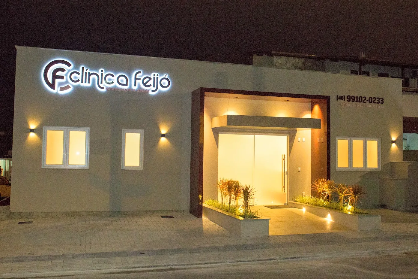 Fachada da Clínica Feijó à noite, com o letreiro aceso e a entrada iluminada